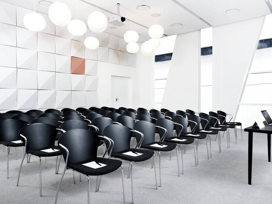Une salle de conférence avec des rangées de chaises noires, un projecteur et un ordinateur portable posé sur une table.