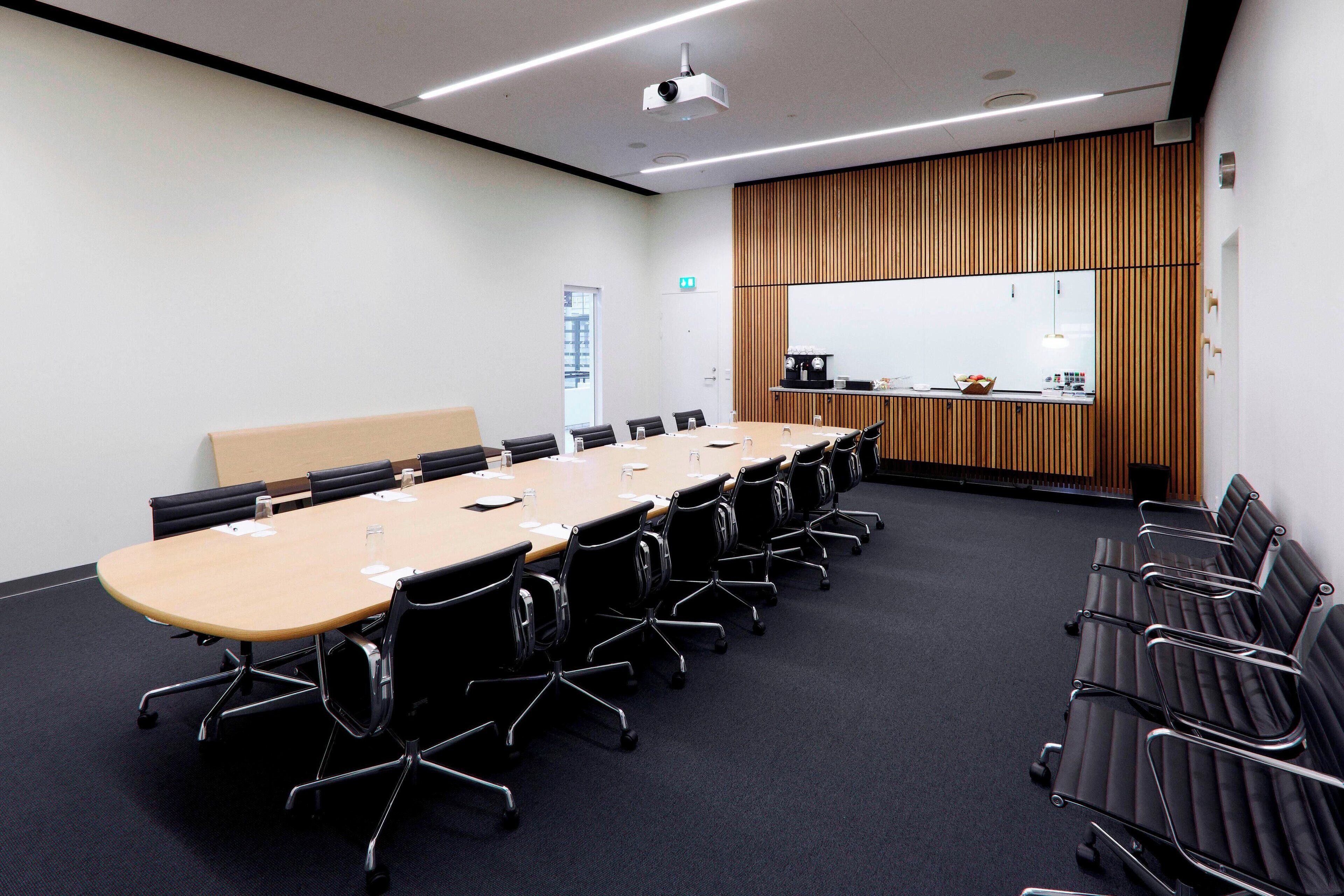 A conference room with a long table, chairs, a projector, and a kitchenette.