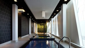 A modern indoor swimming pool with a clear view of the pool area, surrounded by dark tiled walls and large windows. - AC Hotel by Marriott Bella Sky Copenhagen (Copenhagen)