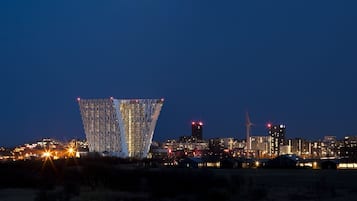 Un paisaje urbano nocturno con un edificio destacado que presenta una fachada única con patrones iluminados.
