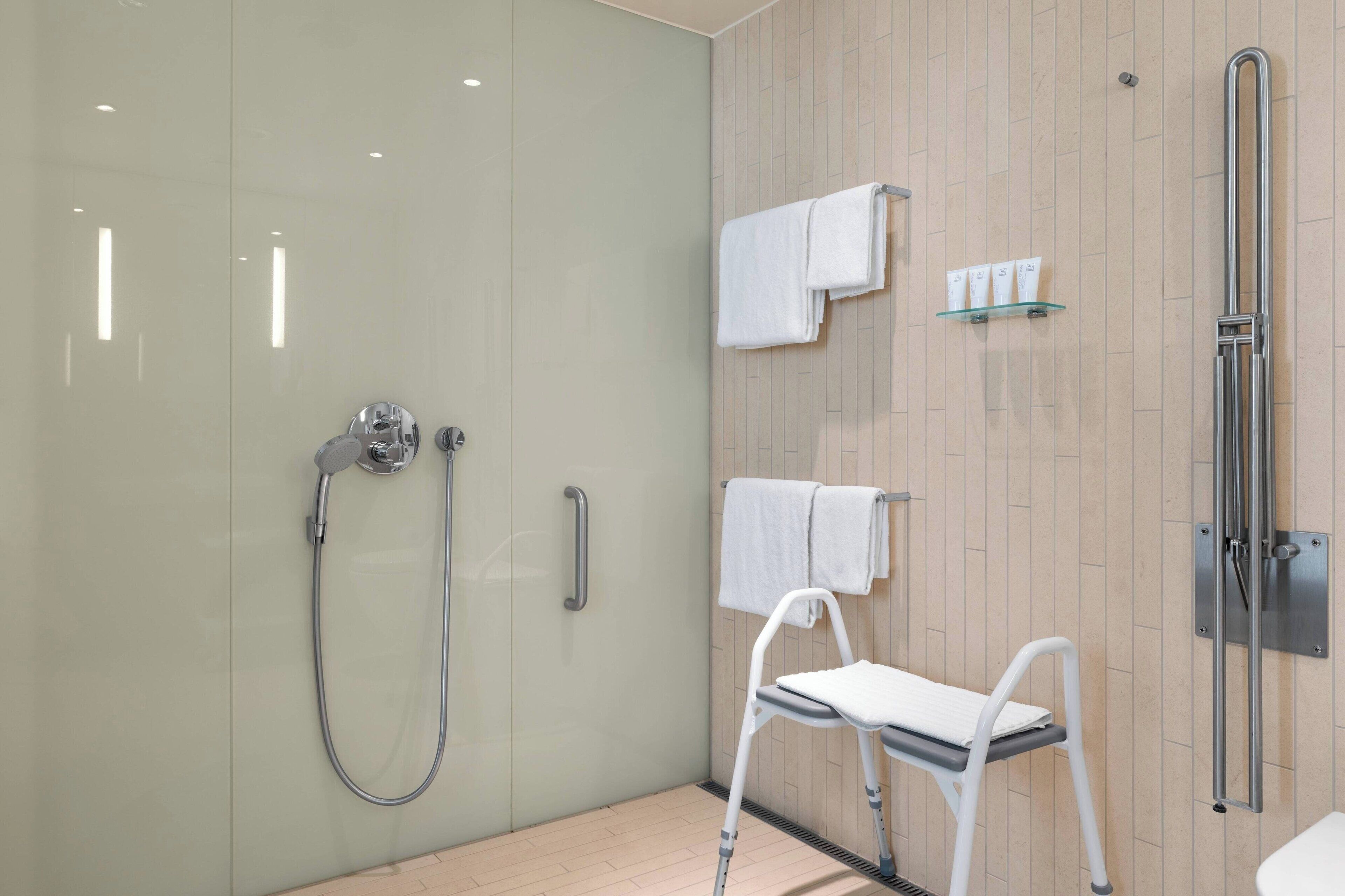 Un bagno moderno con cabina doccia in vetro, una sedia bianca e uno scaffale in vetro con articoli da toilette.