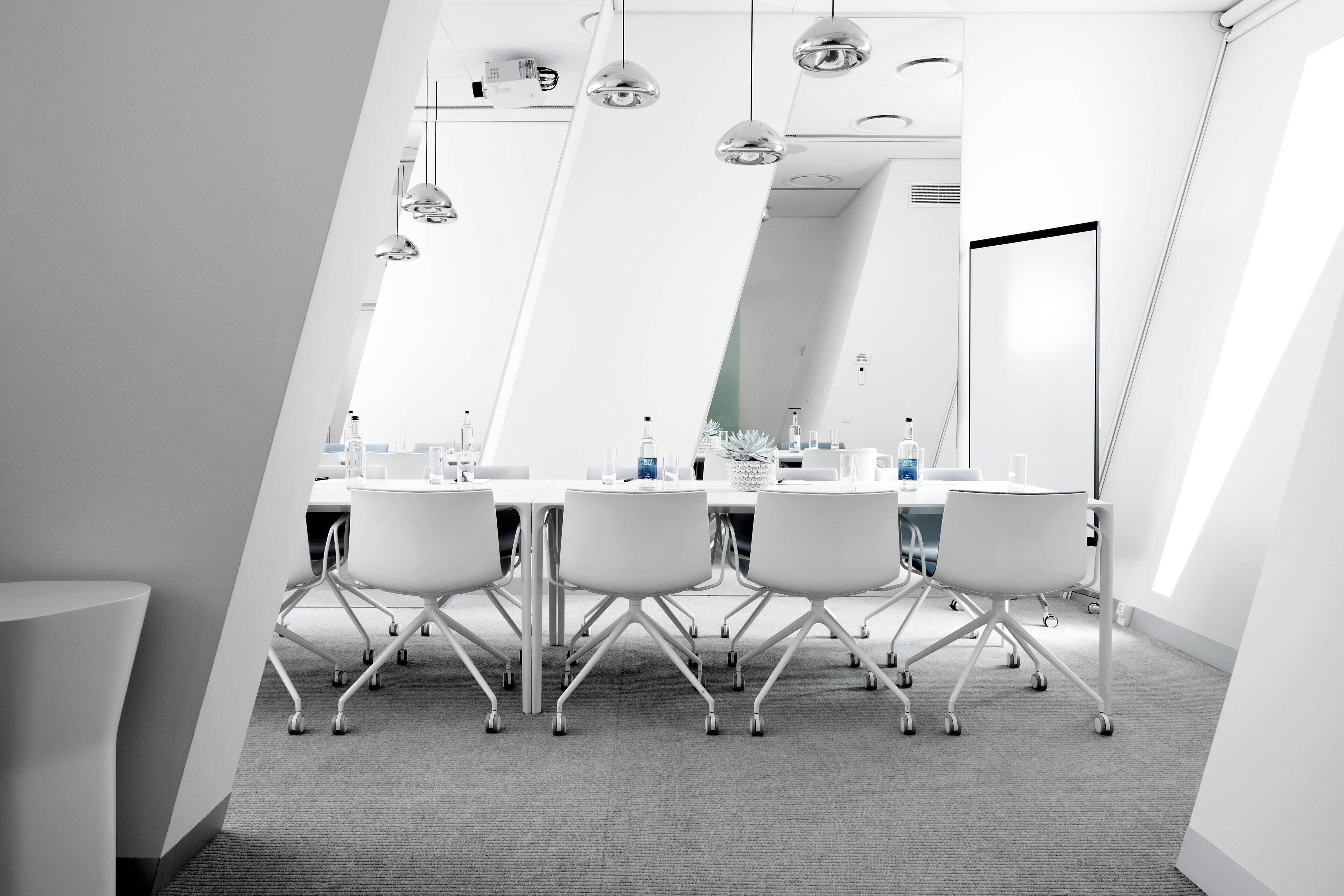 A modern conference room with a white table, four chairs, and a large mirror.
