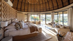 Une chambre spacieuse avec un grand lit, un coin salon avec vue et un coin repas agrémenté d’une bouteille de champagne.