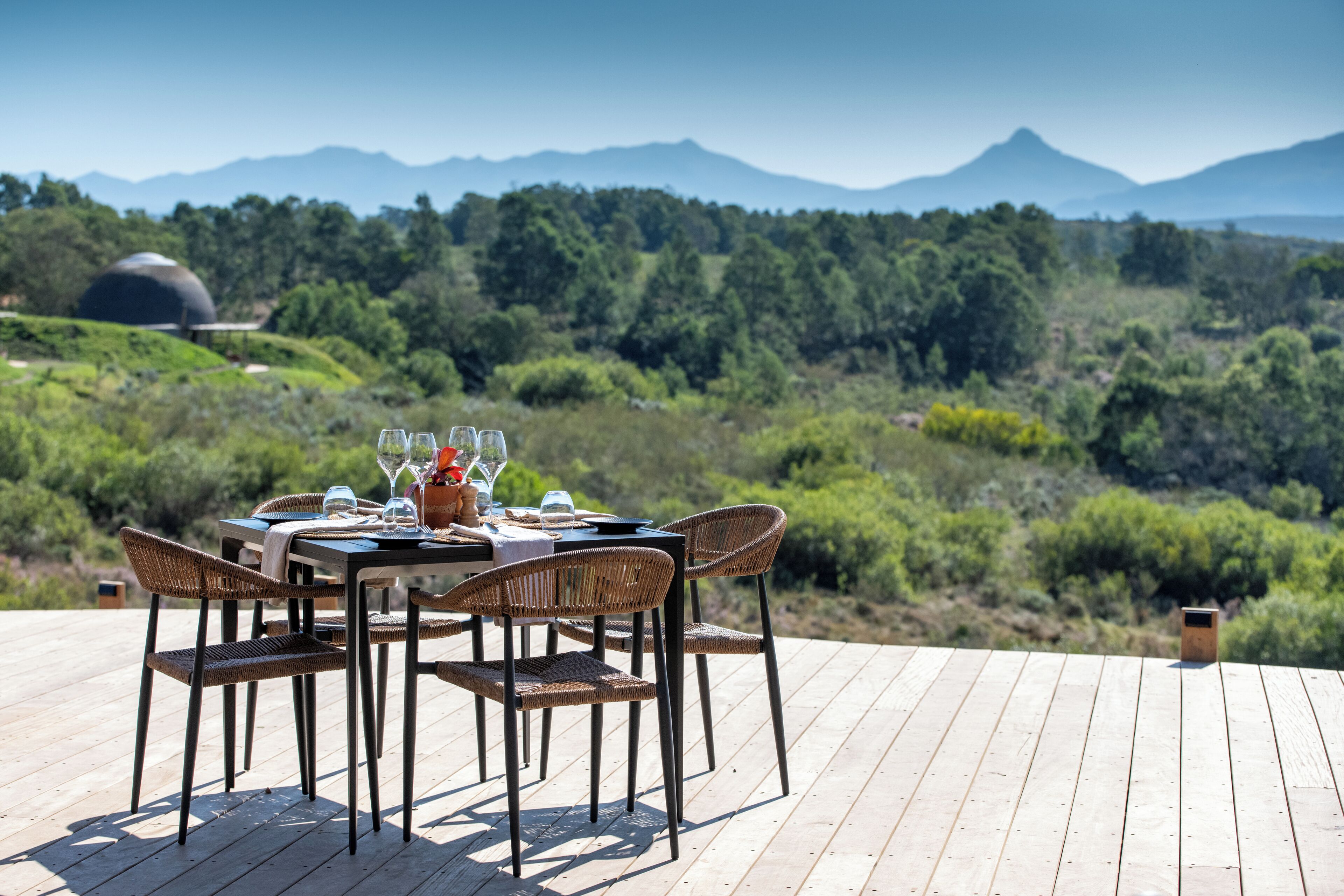 A dining table with wicker chairs and a view of a mountainous landscape.