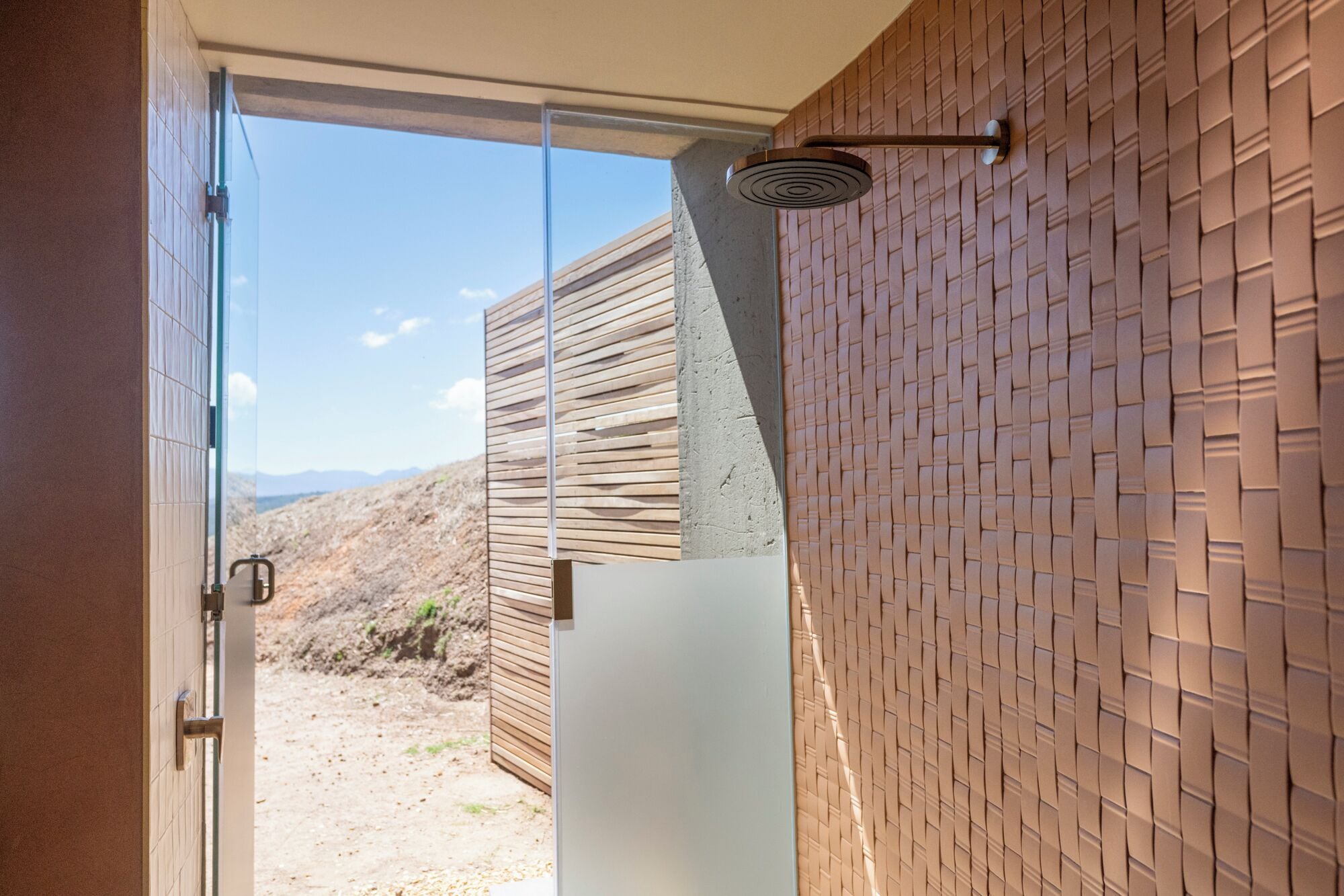 A modern bathroom with a glass door leading to a view of a desert landscape.