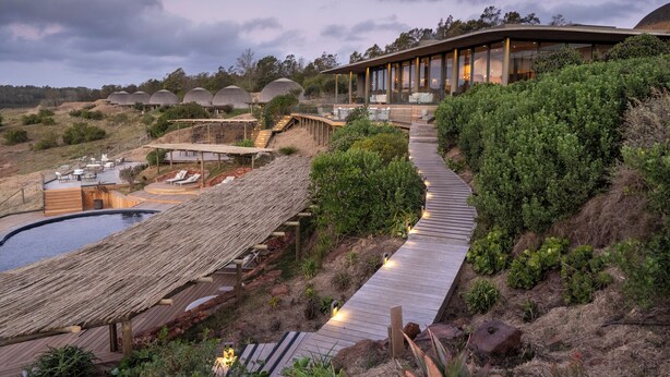 Un complexe hôtelier doté d’une terrasse en bois, d’une piscine et de bungalows aux toits de chaume.