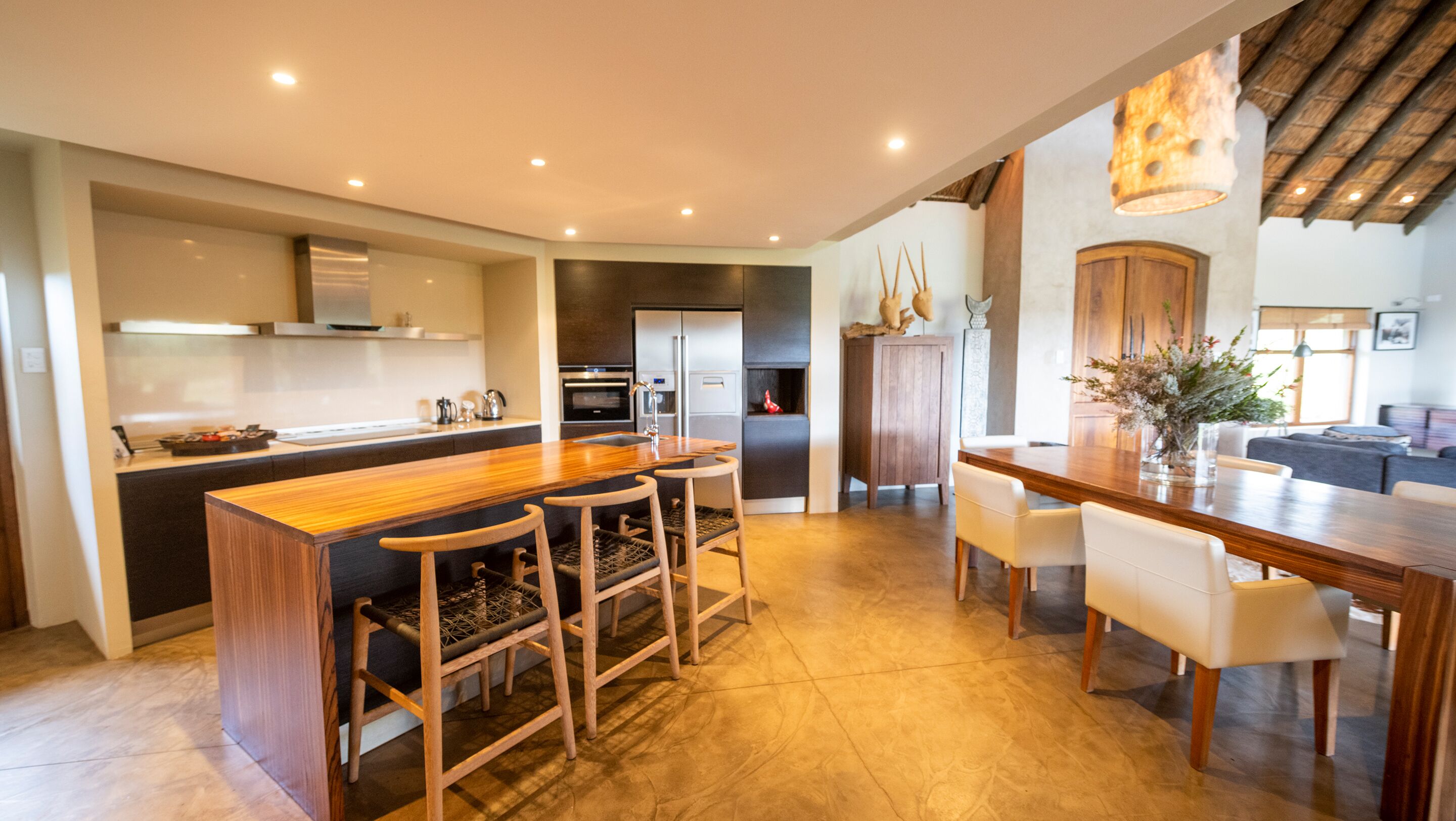 A modern kitchen with a central island, bar stools, and a dining area with a wooden table and chairs.