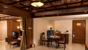 A hotel room with a wooden ceiling, a television, a desk with a computer, a dining table with chairs, and a door with a sign.