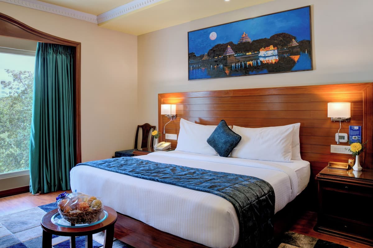 Een hotelkamer met een groot bed, een nachtkastje met een lamp, een schilderij van een nachtelijke scène en een raam met gordijnen.