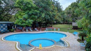 A swimming pool with a circular section, surrounded by a tiled deck and benches.