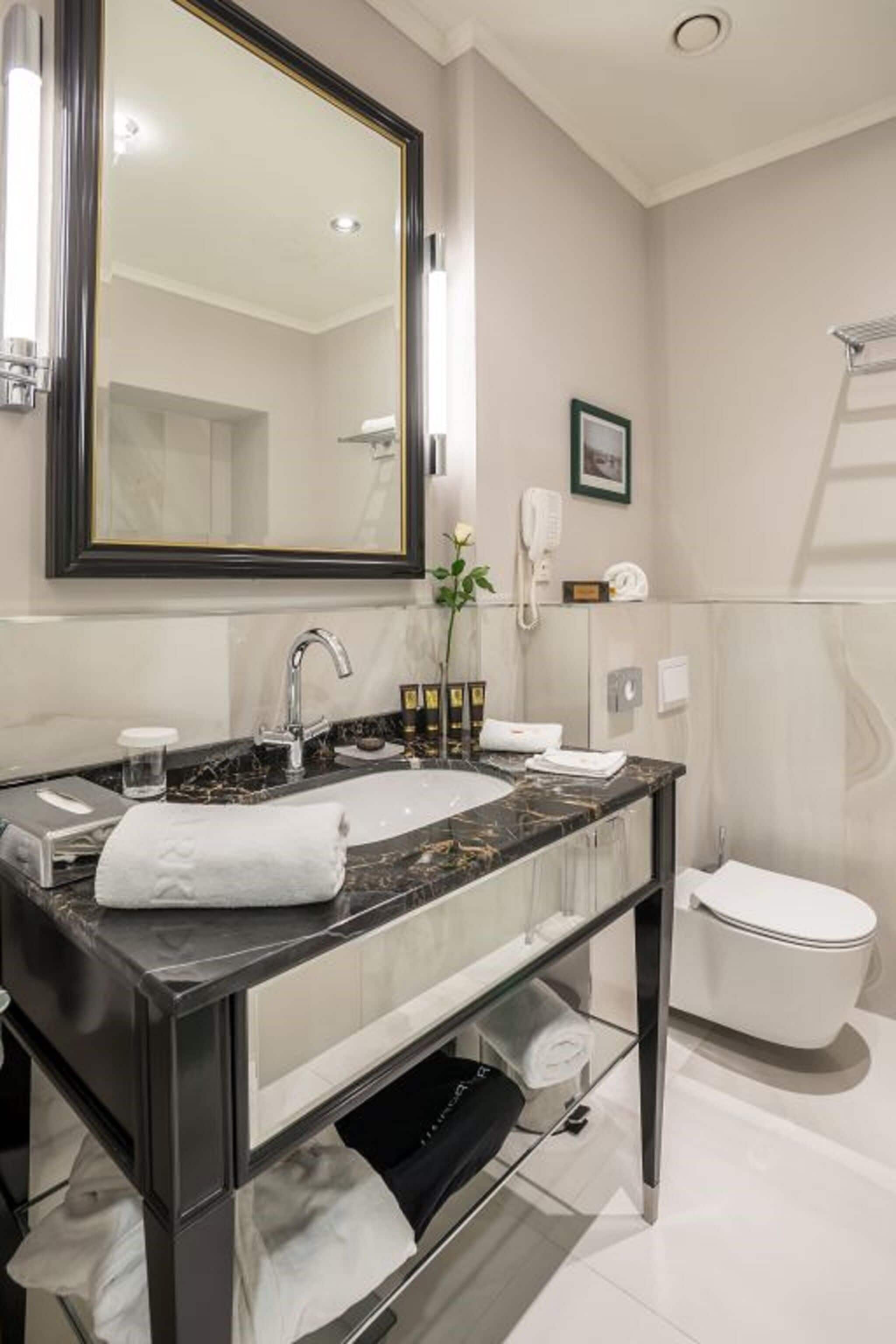 Un baño moderno con lavamanos de mármol, un espejo grande, inodoro y zona de ducha.