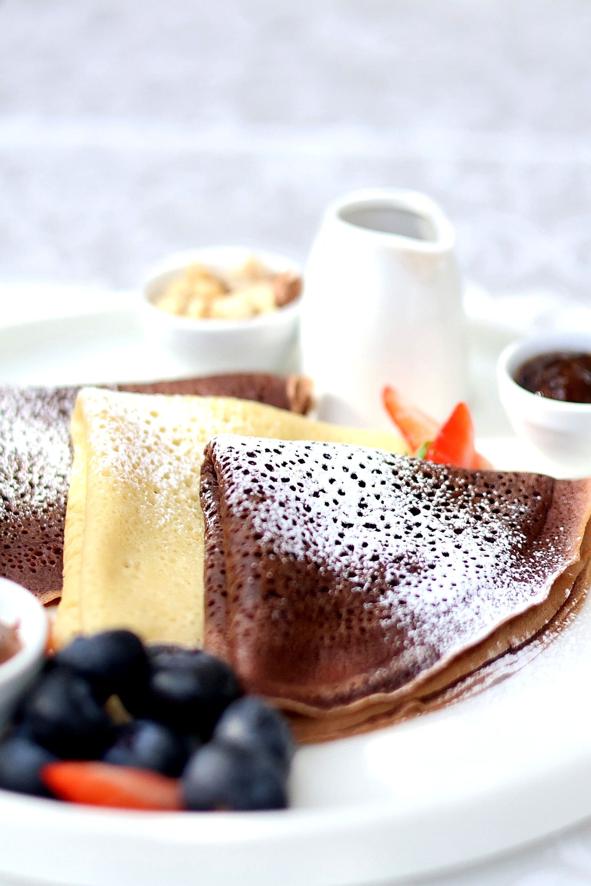 A plate with crepes, blueberries, and a small bowl of syrup.