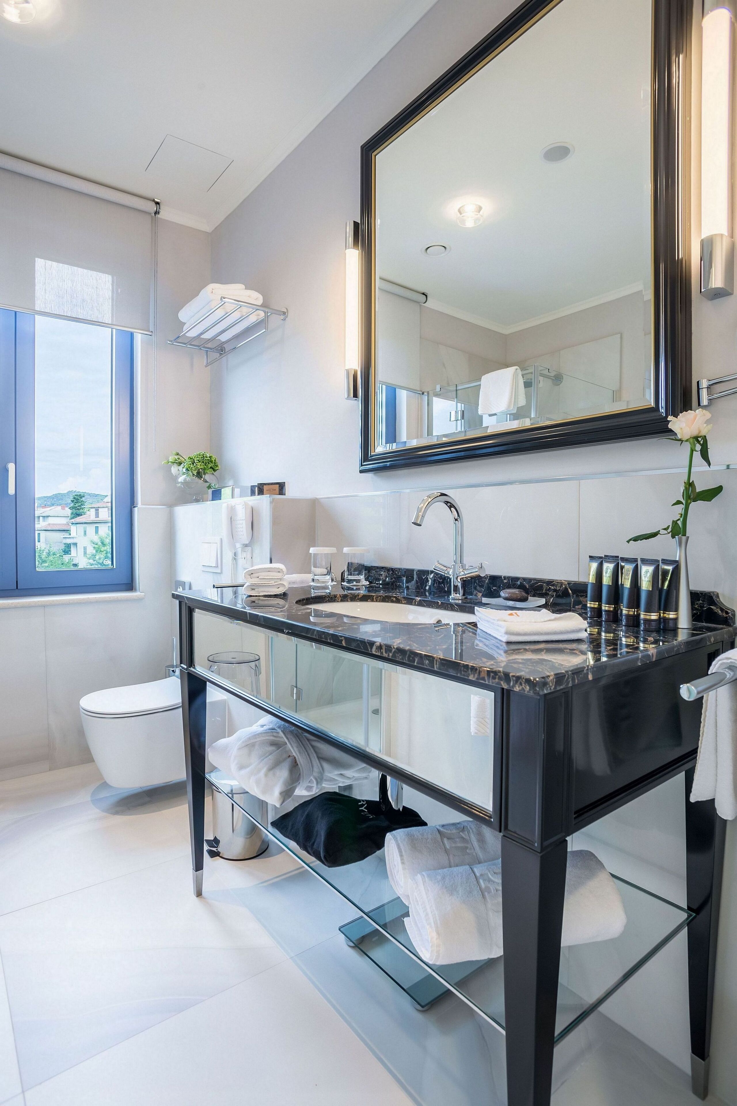 A modern bathroom with a large mirror, a glass sink, and a toilet.