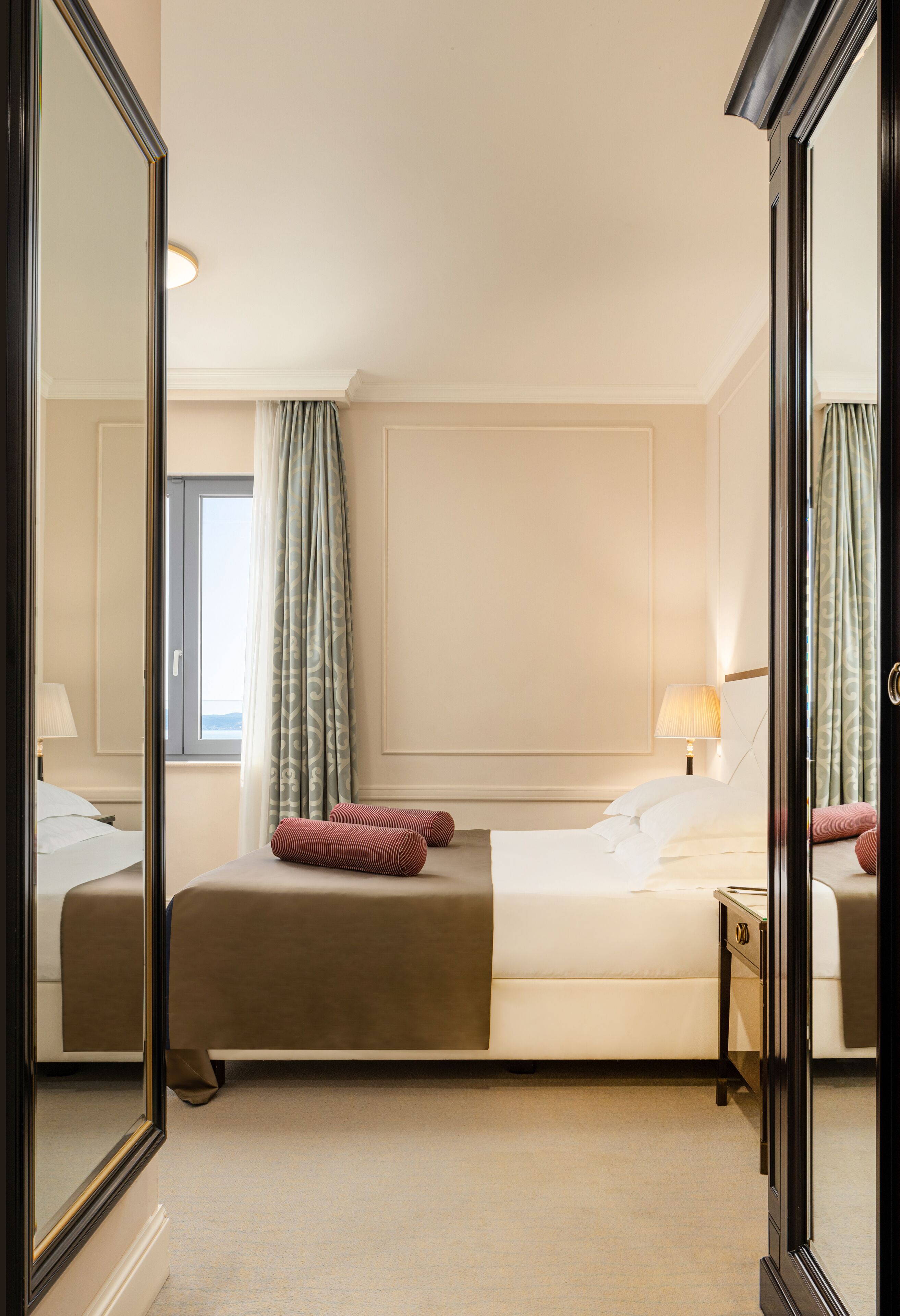 A hotel room with a large bed, a bedside table, a lamp, and a window with curtains.