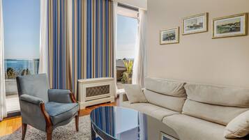 A living room with a view of the sea, a blue armchair, a beige sofa, and a glass coffee table.