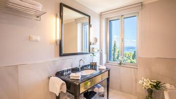 A modern bathroom with a marble sink, large mirror, and a view of the sea through a window.
