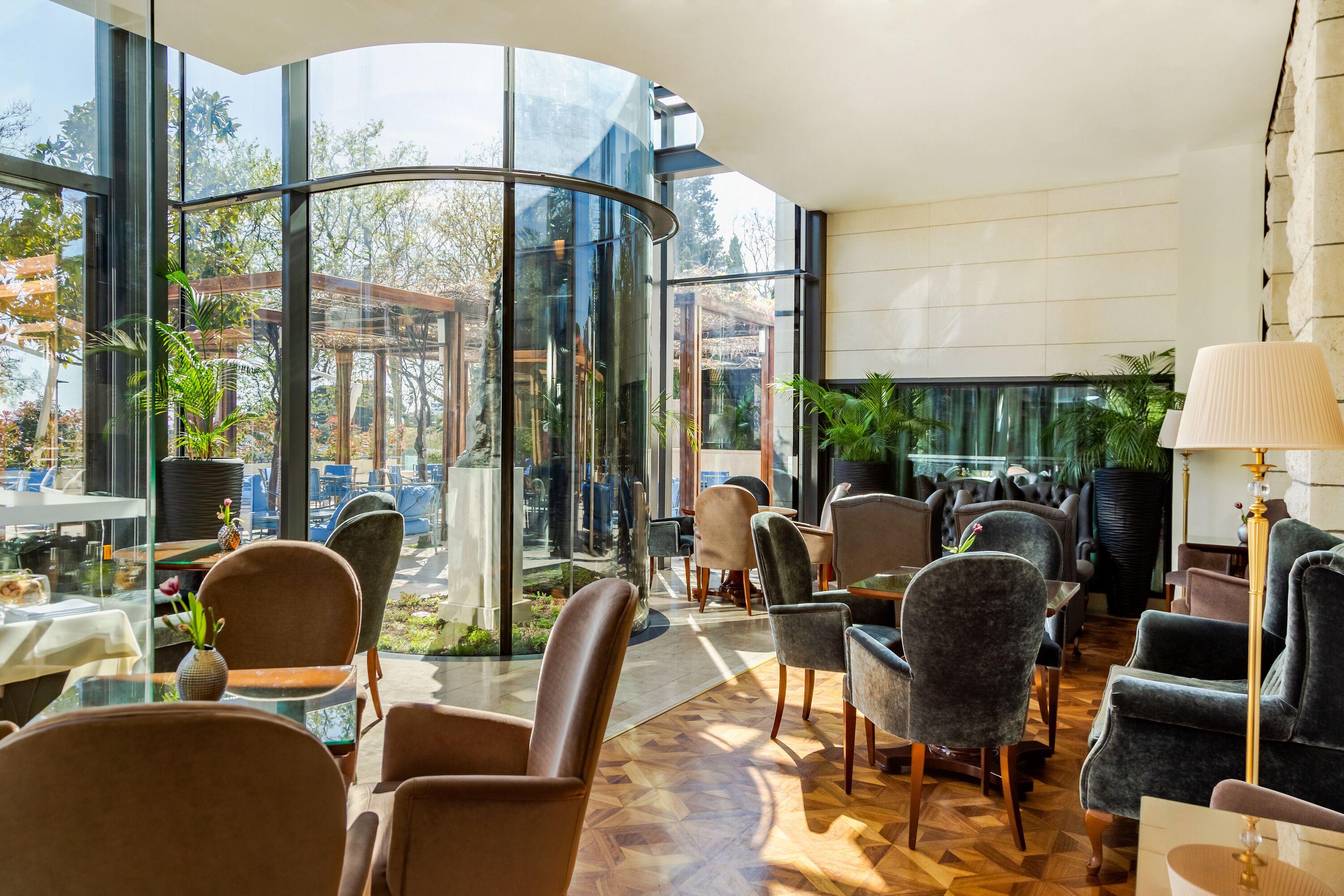 A modern interior with curved glass walls, comfortable seating, and indoor plants.