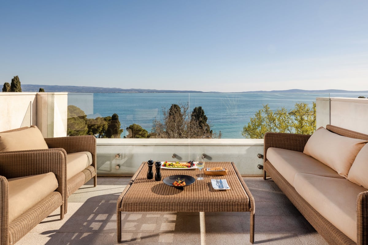 A balcony with wicker furniture, a dining table, and a view of the sea.