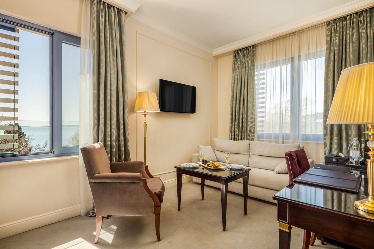 A hotel room with a sofa, armchair, and a small table with a fruit plate and glasses.