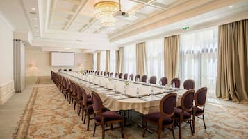 Un salón de conferencias con una larga mesa, sillas, una pantalla de proyector y un gran ventanal con cortinas.