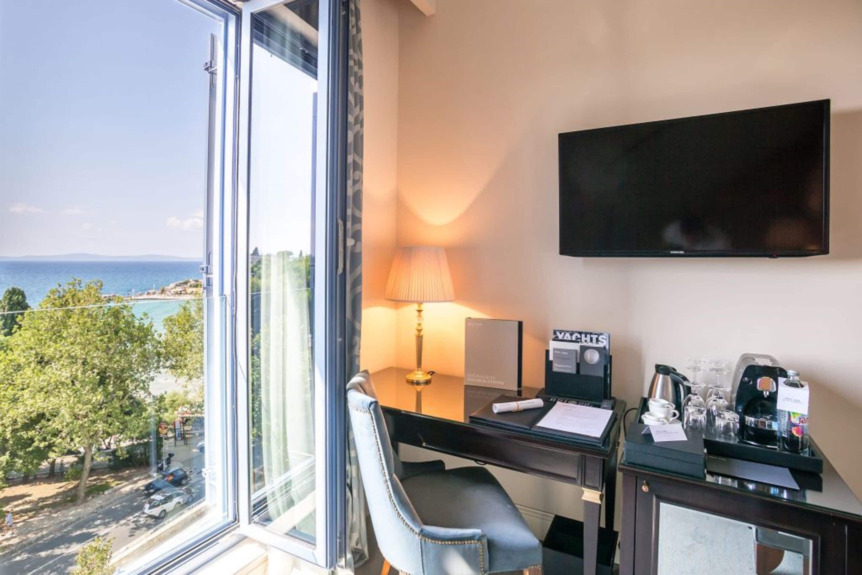 A hotel room with a desk, chair, TV, and a view of the sea.