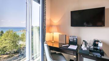 A hotel room with a desk, chair, TV, and a view of the sea.