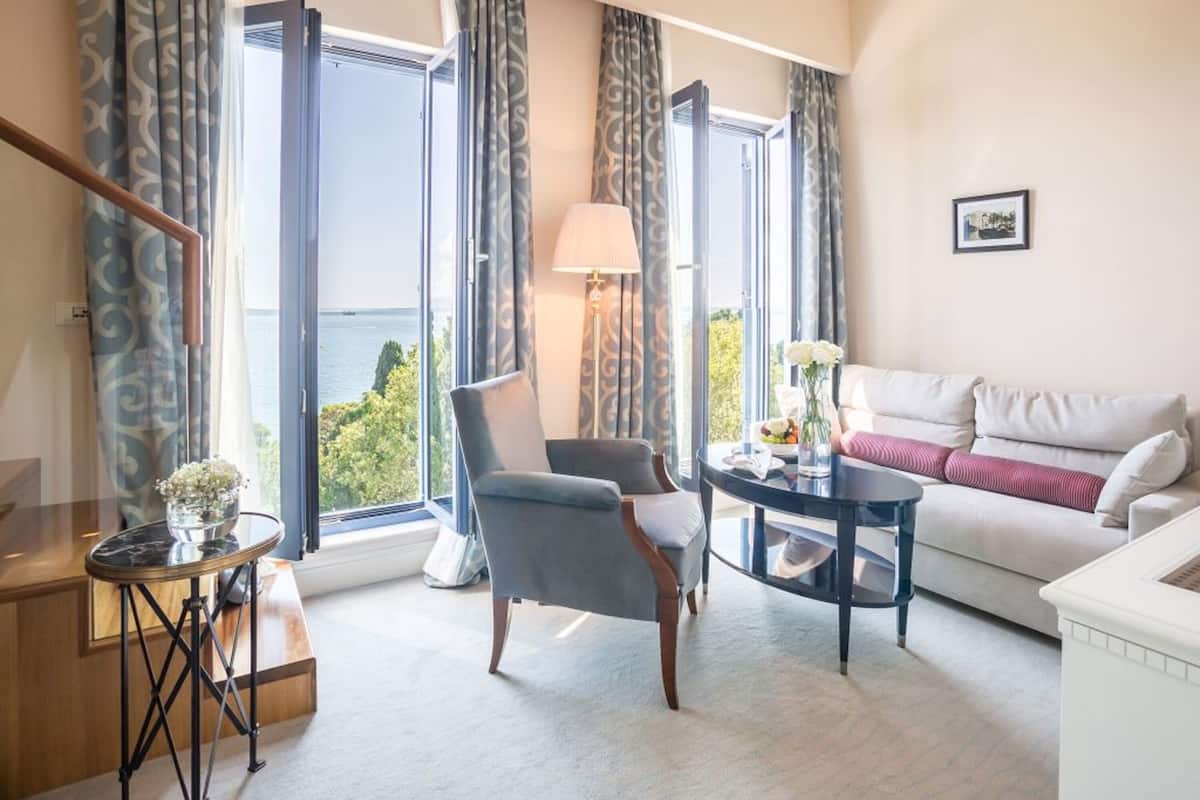A modern living room with a sofa, a chair, a table, and a lamp. Large windows offer a view of the outdoors.