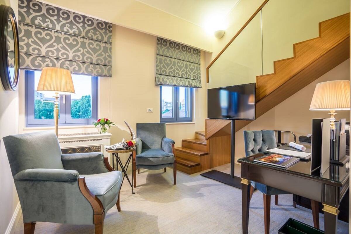 A living room with a sofa, two armchairs, a coffee table, a TV, and a staircase.