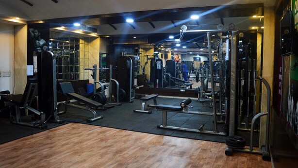 Uma academia com diversos equipamentos de exercício, espelhos e piso de madeira.