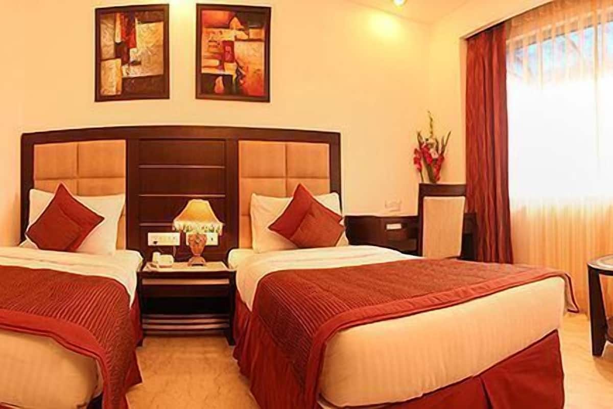 A hotel room with two beds, a desk, a chair, and a window with curtains.
