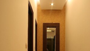 Um corredor com parede estampada, porta de madeira com espelho e chão de mármore.