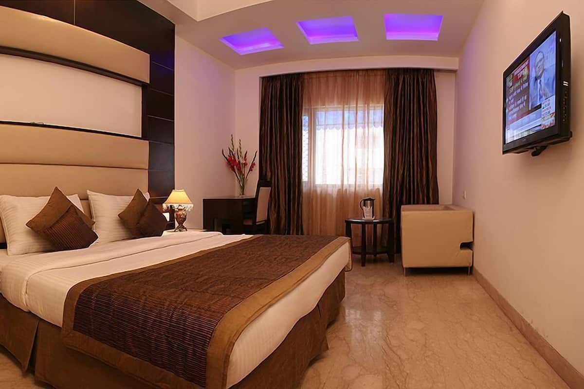 A hotel room with a large bed, a desk, a chair, a TV, and a lamp.