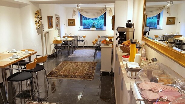 Une salle à manger d’hôtel avec plusieurs tables et chaises, un buffet proposant divers plats, et une fenêtre donnant sur un paysage verdoyant.
