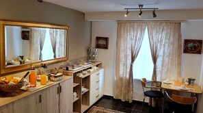 Ein Hotelzimmer mit Frühstückstresen, einem großen Spiegel, einem Esstisch mit Stühlen und einem blickdichten Fenster.