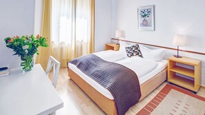 Ein ordentlich eingerichtetes Hotelzimmer mit einem Bett, Nachttischen, einem Schreibtisch und einem Stuhl.