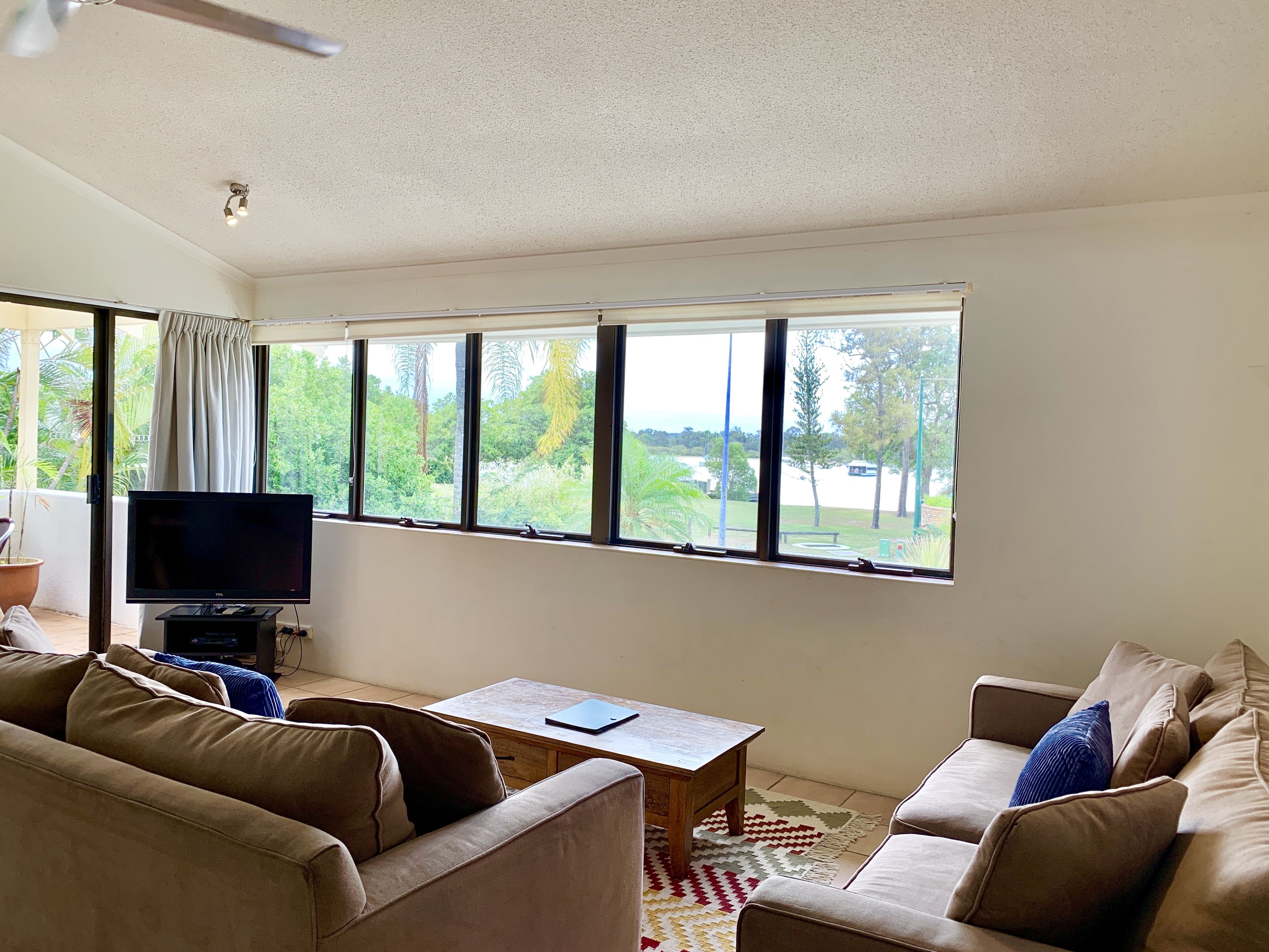 A living room with a TV, two sofas, a coffee table, and a view of greenery outside.