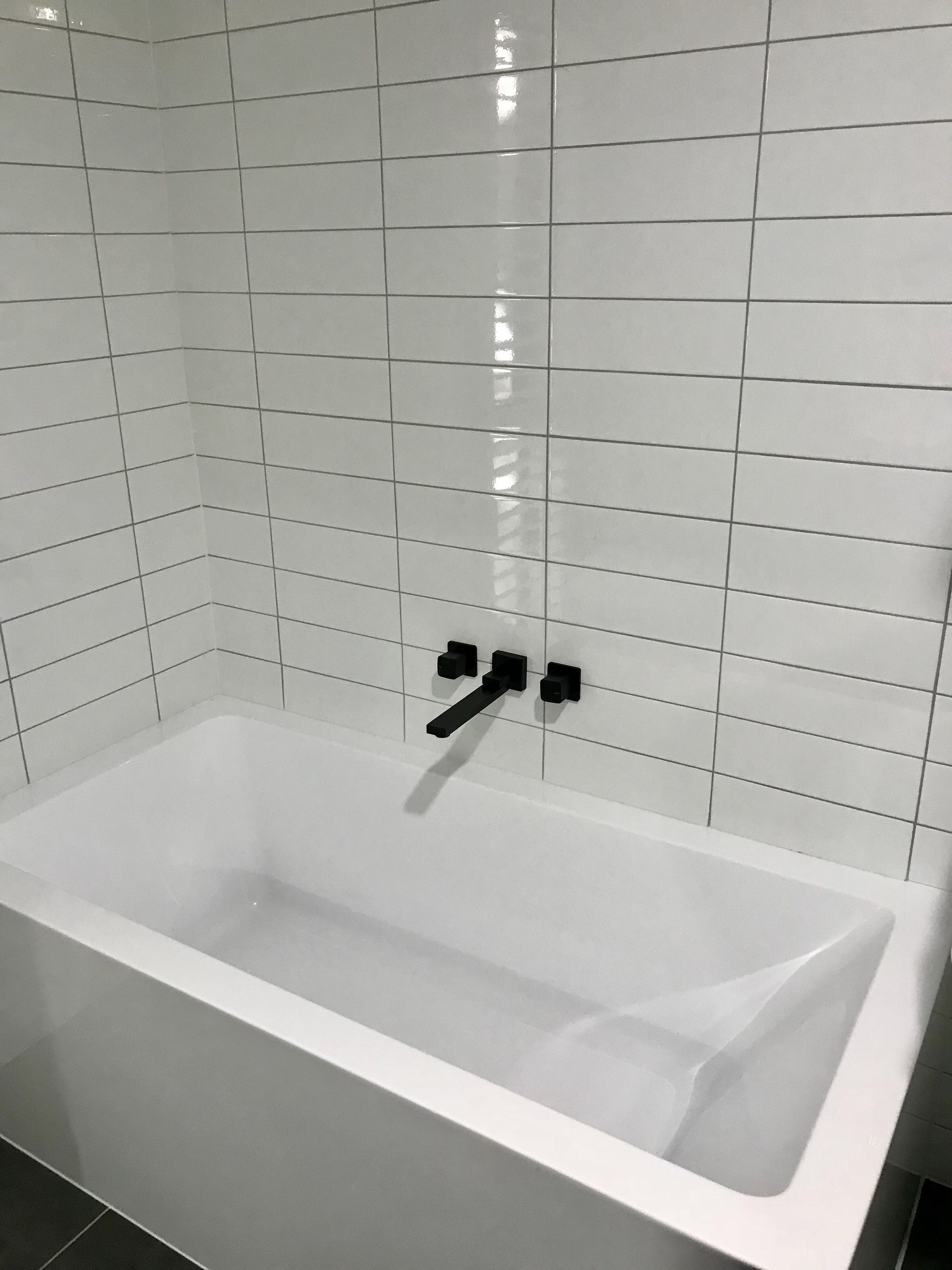 A white bathtub with black fixtures in a bathroom with white tiled walls.