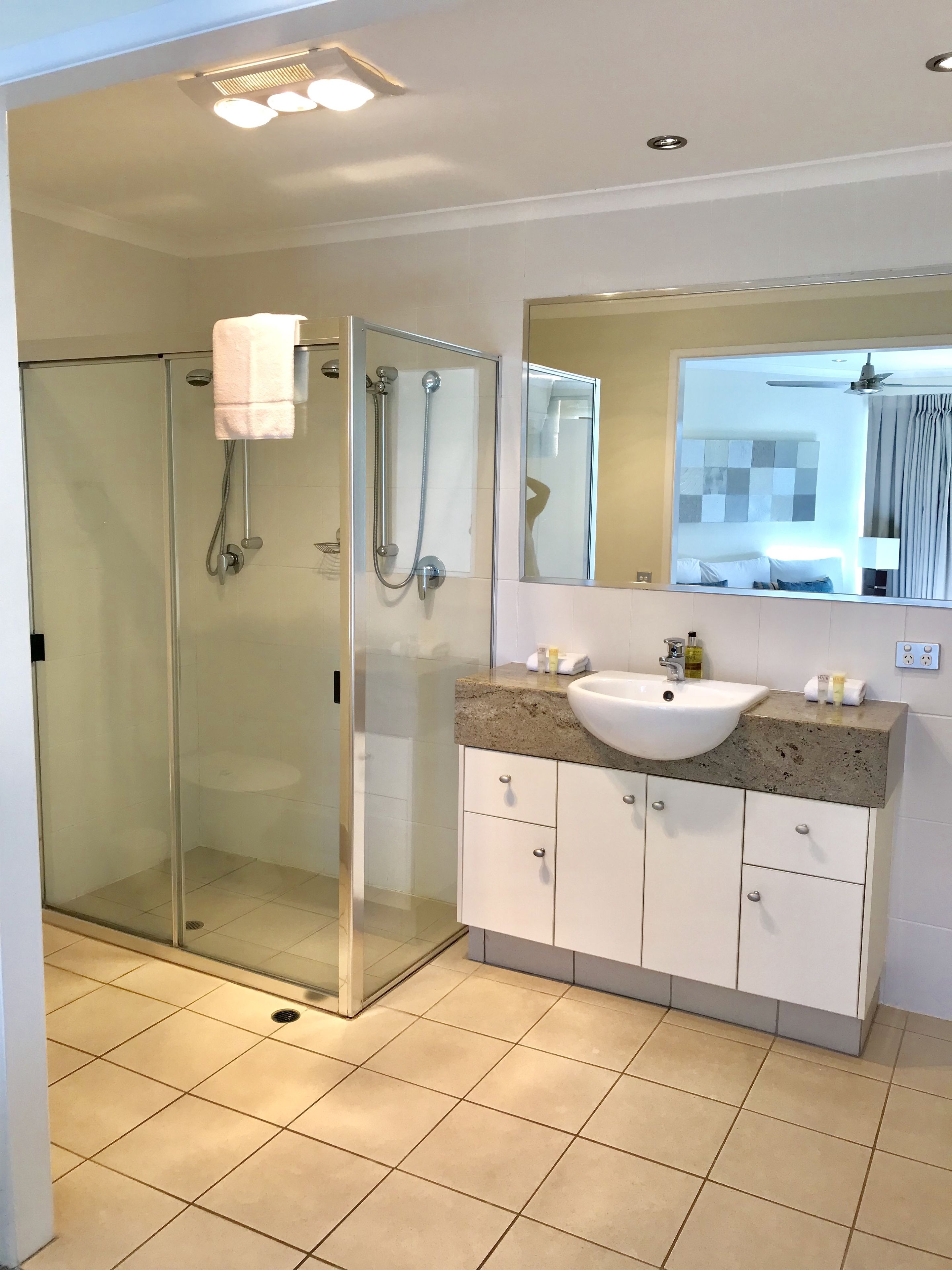 A modern bathroom with a glass-enclosed shower, a white sink, and a large mirror.