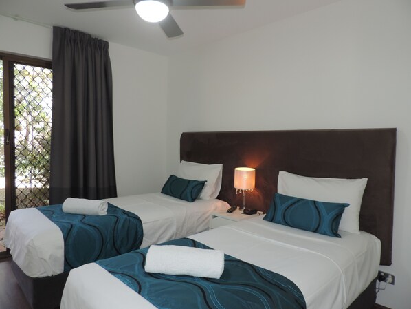 A hotel room with two beds, a nightstand, a lamp, and a ceiling fan.