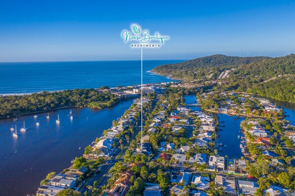 An aerial view of Noosa Boutique Apartments with a marina, dense greenery, and a clear blue sky.