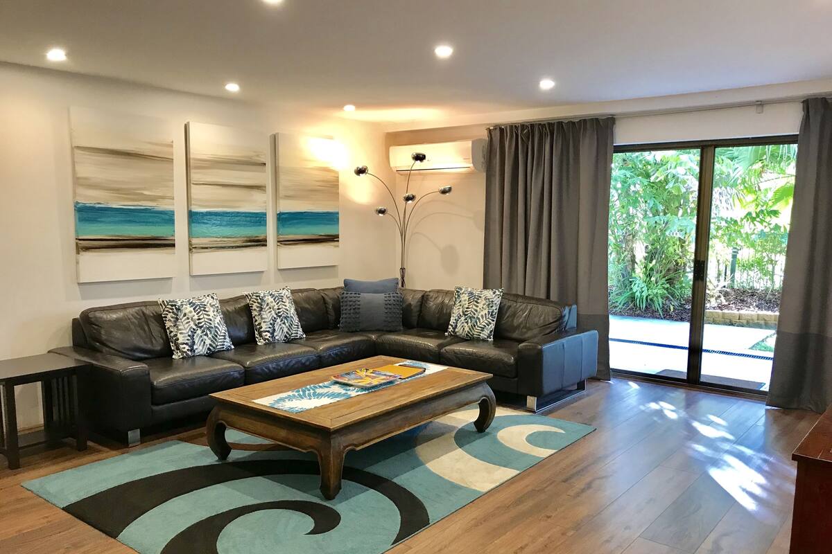 A modern living room with a leather sectional sofa, a wooden coffee table, and a large window with curtains.