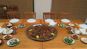 A dining table set for a meal with various dishes, including a large platter of food at the center, surrounded by smaller plates of salads and sides.