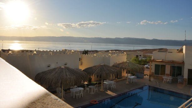 A rooftop pool area with thatched umbrellas, lounge chairs, and a view of the sea and mountains.