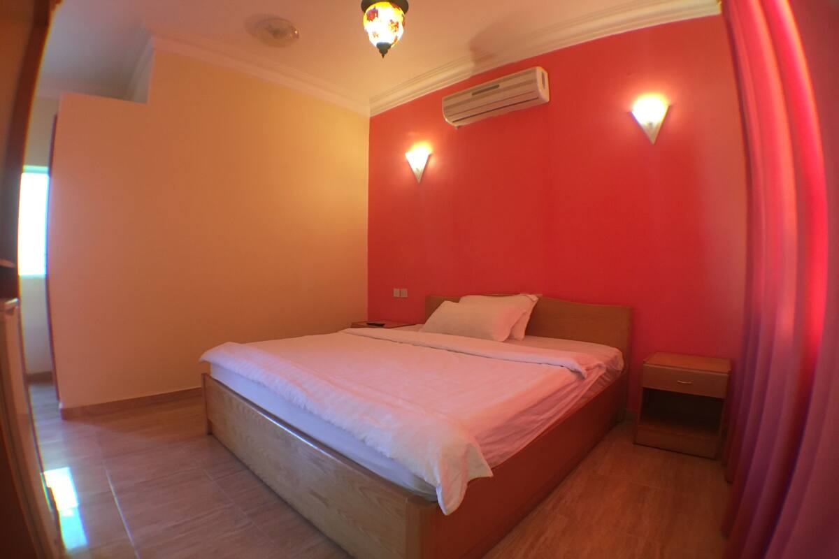 A bedroom with a wooden bed, a nightstand, and a wall-mounted air conditioner.