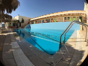 Una piscina con solárium de baldosas y escalera metálica.