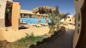A poolside area with lounge chairs, a thatched umbrella, and a building with a blue-tiled wall.