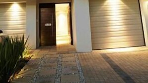 A modern two-story house with a garage, a balcony with a wooden pergola, and a well-lit entrance. - Da Heim Guest House (Cape Town)