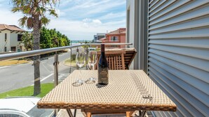 A balcony with a wicker table, a bottle of wine, and two glasses. - Da Heim Guest House (Cape Town)