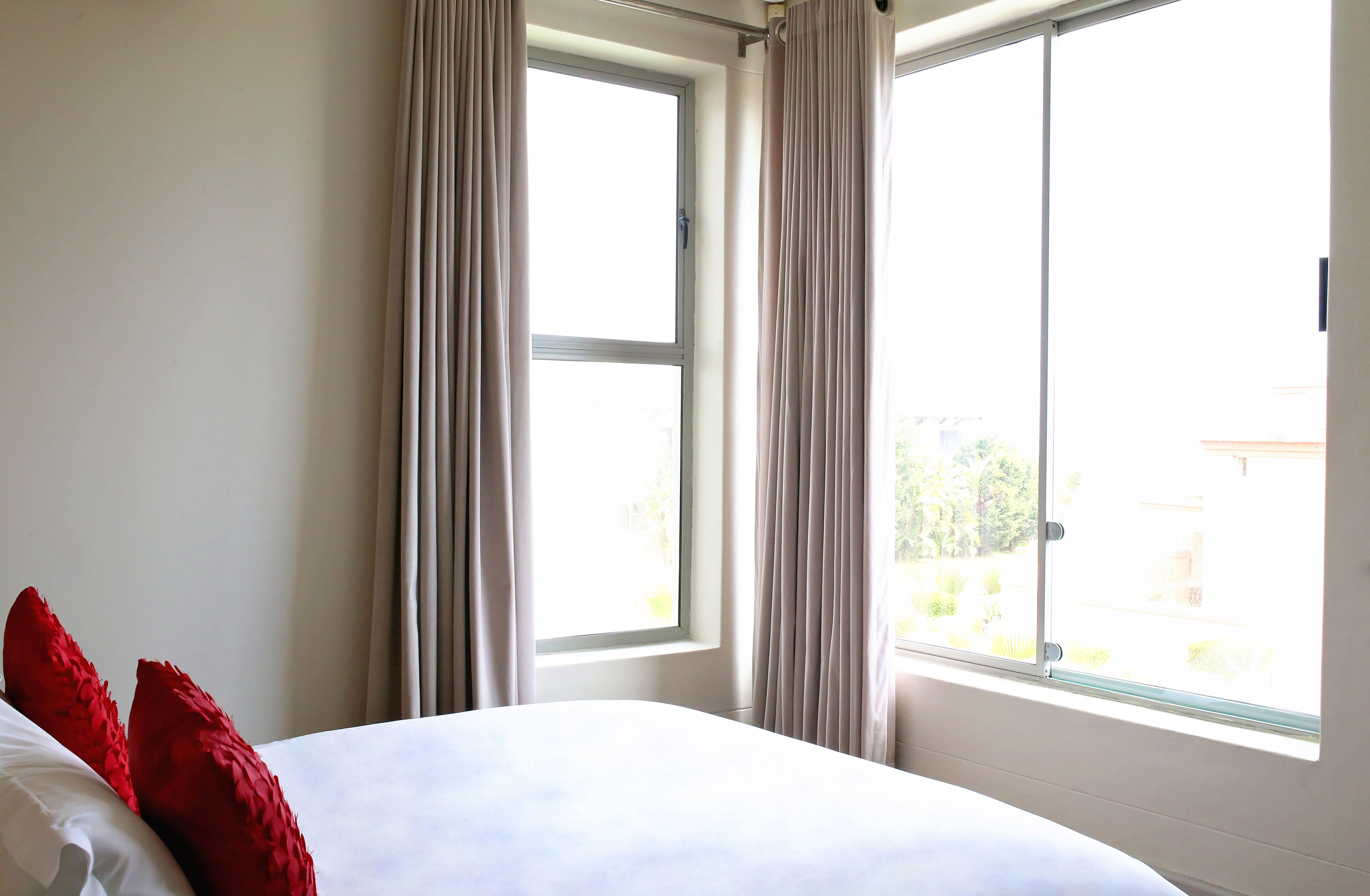 A hotel room with a bed, two windows, and curtains.