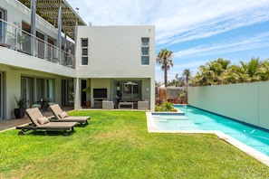 Ein modernes, zweistöckiges Haus mit Swimmingpool, überdachter Terrasse und gepflegtem Rasen.